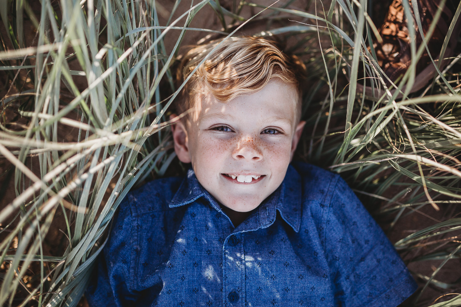 Young blond boy smiling while laying in grass at Caves Beach