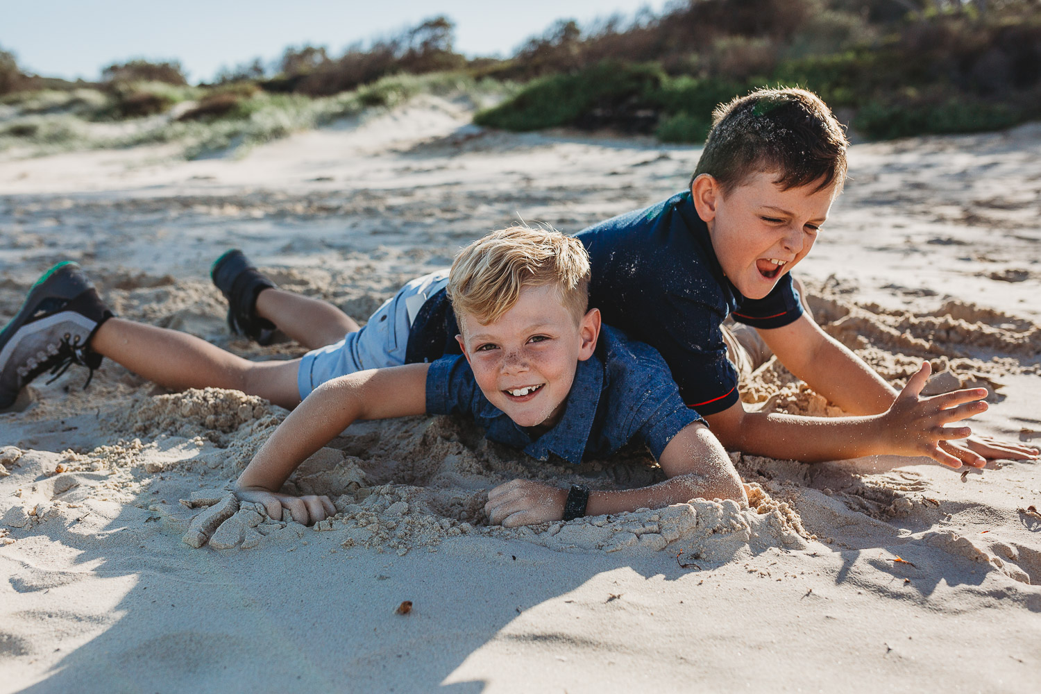Boys smiling and laughing while wrestling at the beach