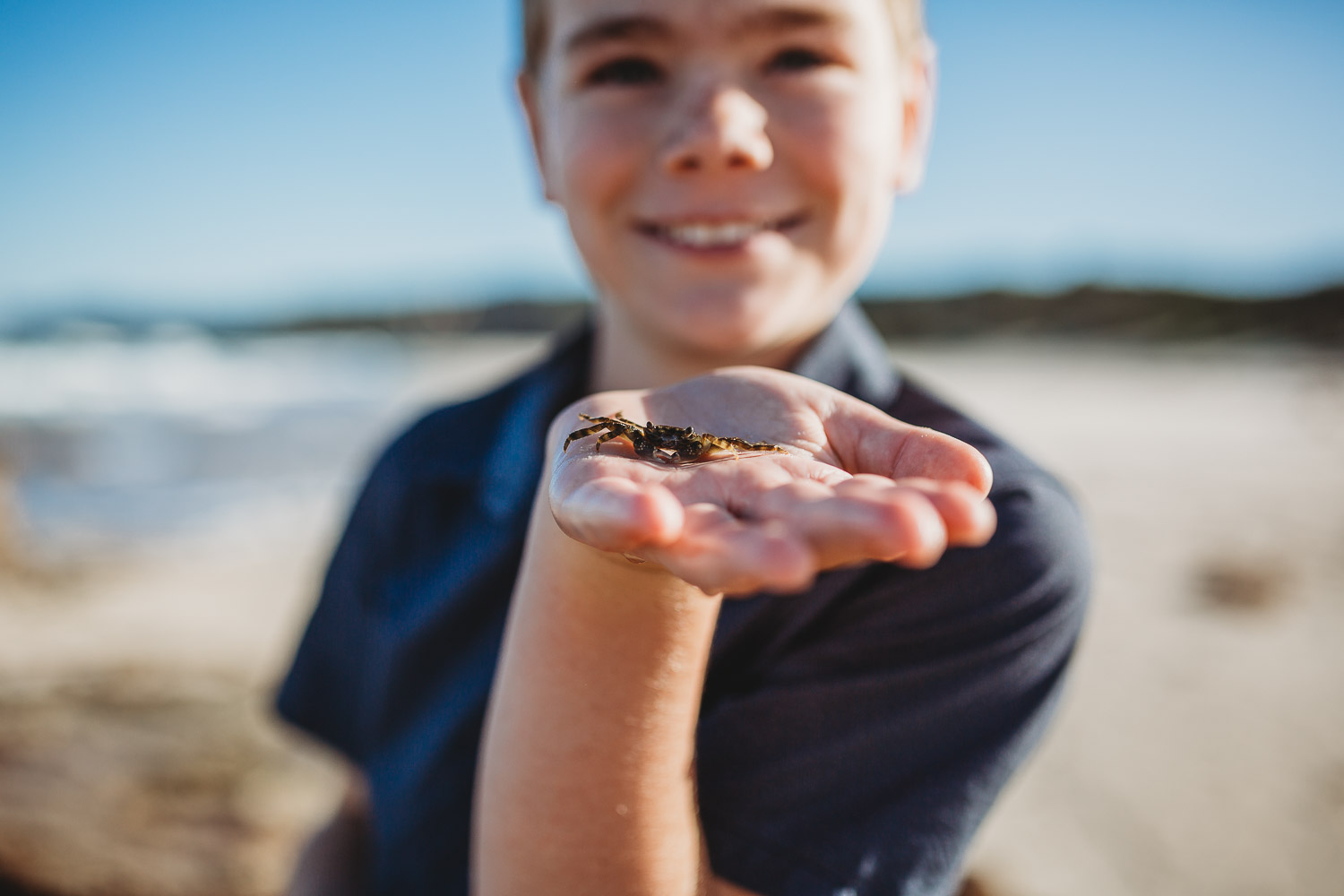 Young boy smiling holding small crab at the beach