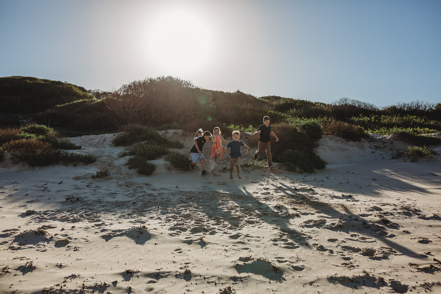 Children running down a sand dune at Caves beach