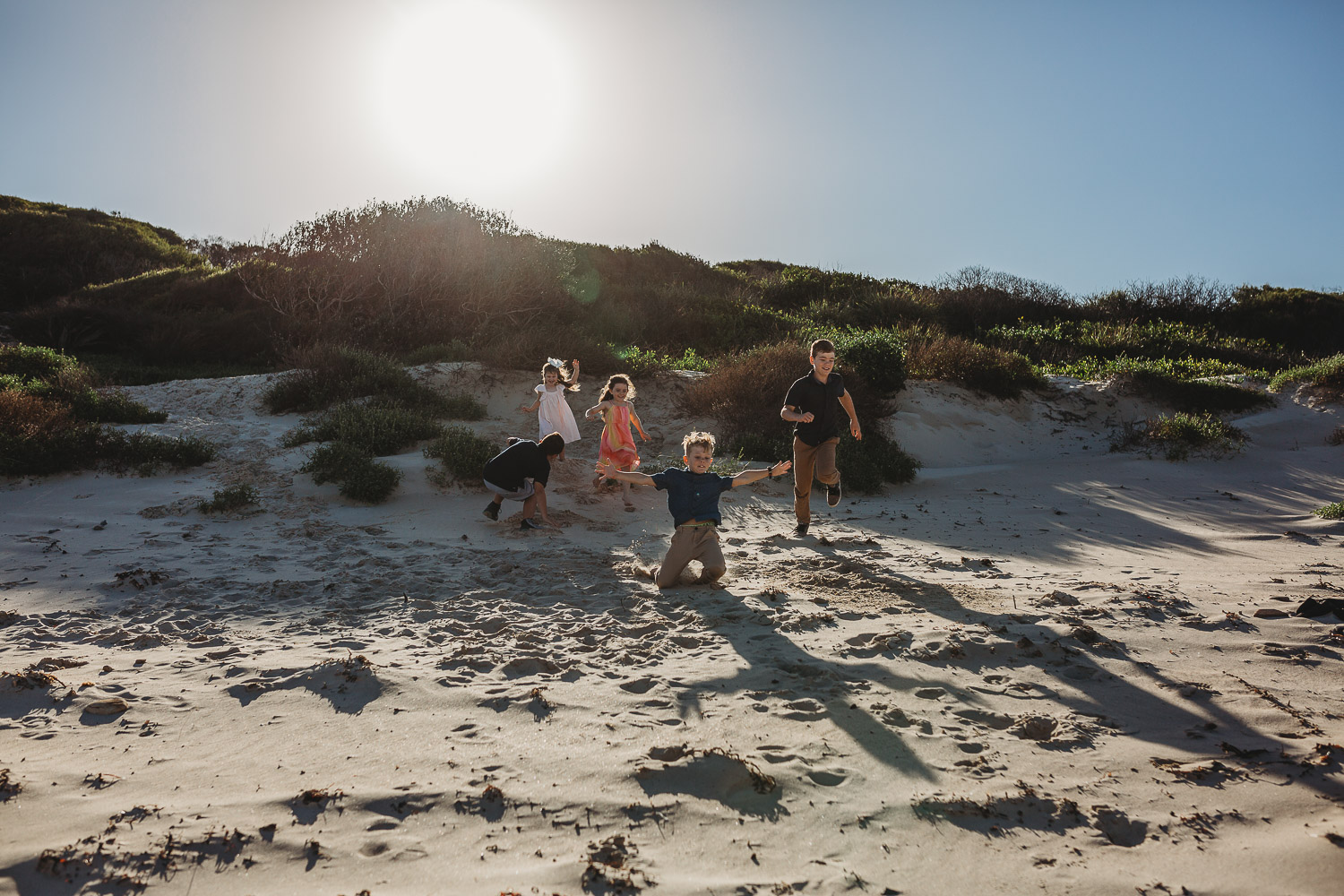 Children racing down a sand dune at the beach
