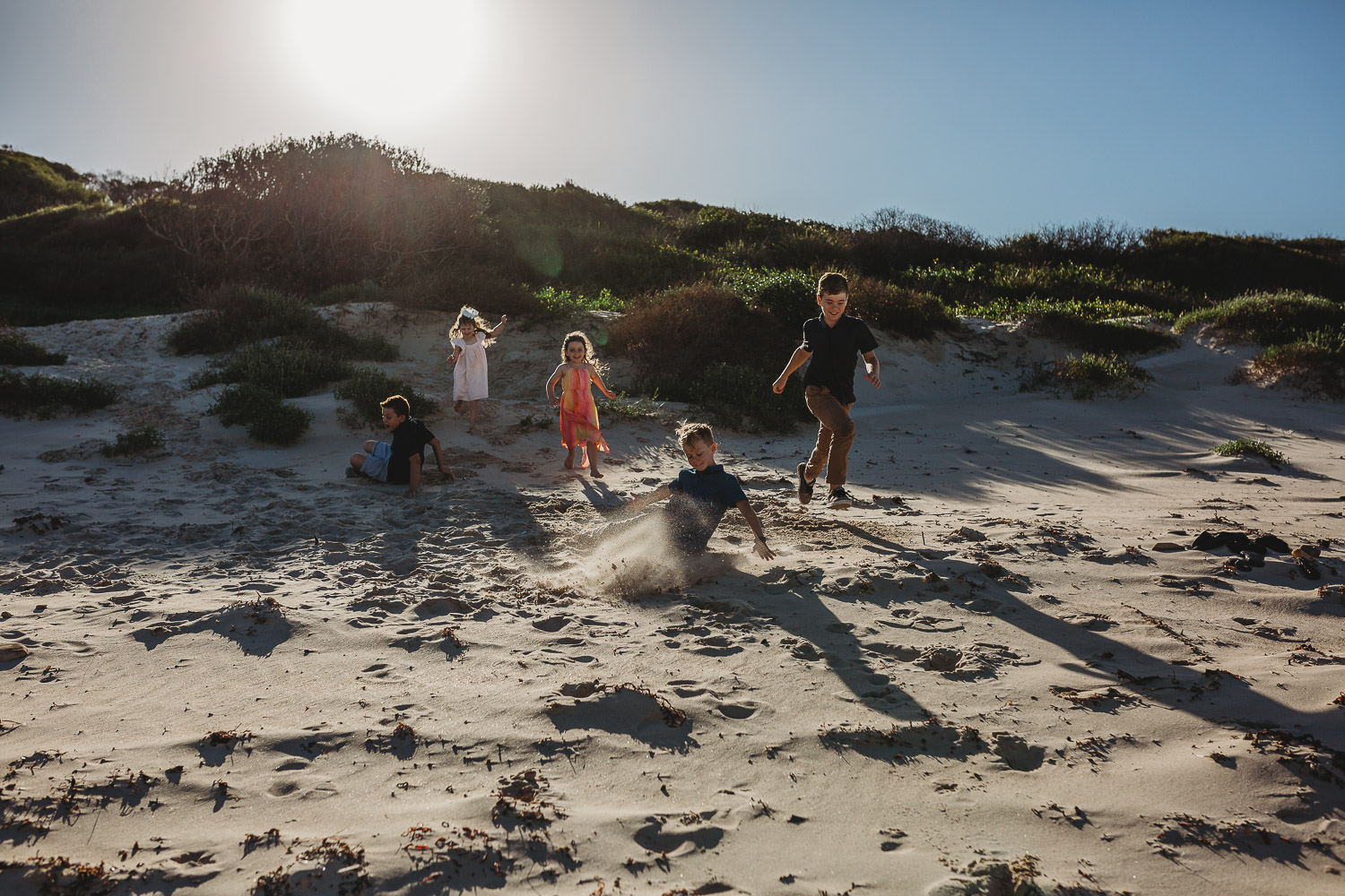 Children running down a sand dune at the beach