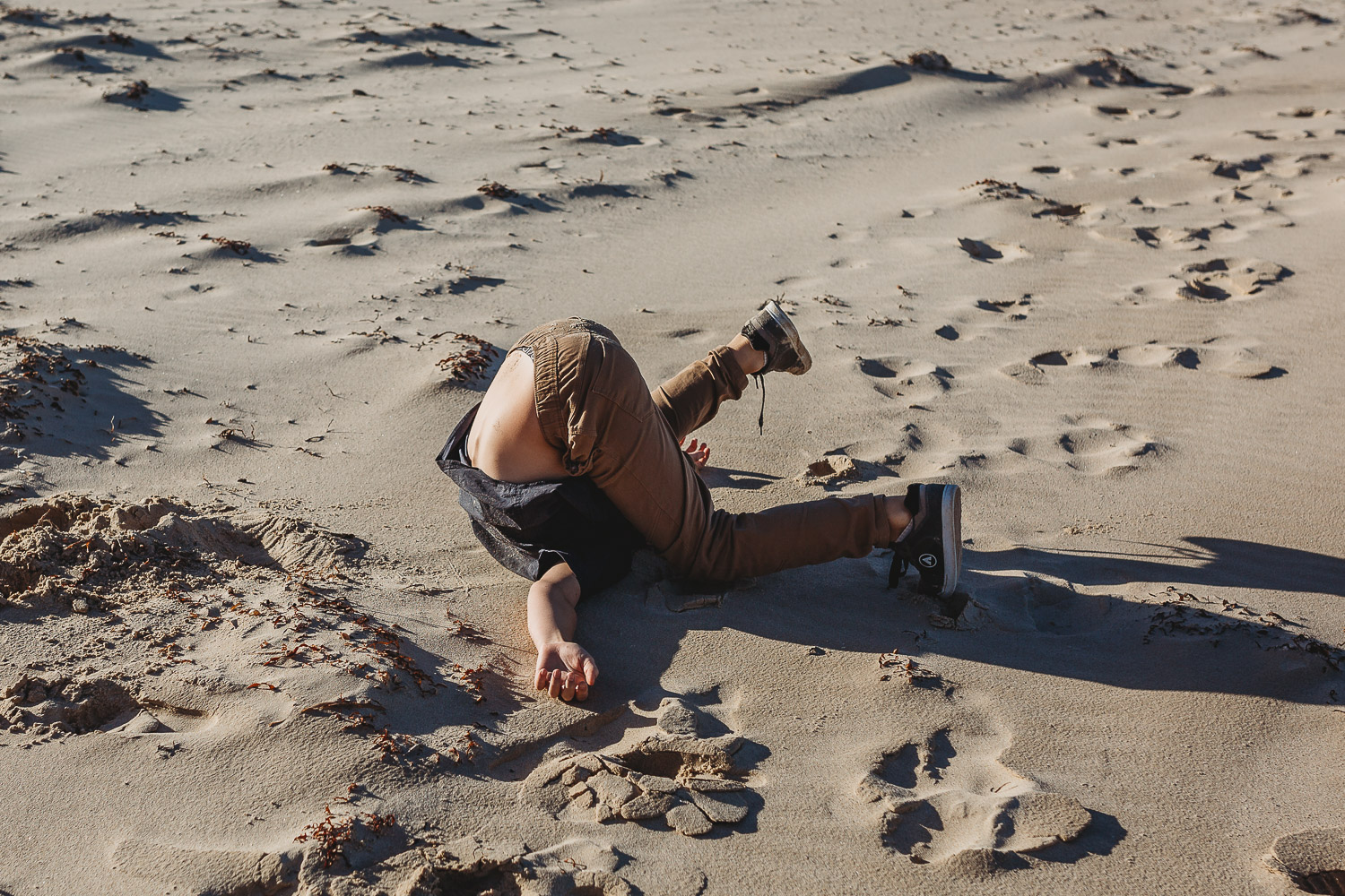 Boy fallen over on the sand in a humourous position