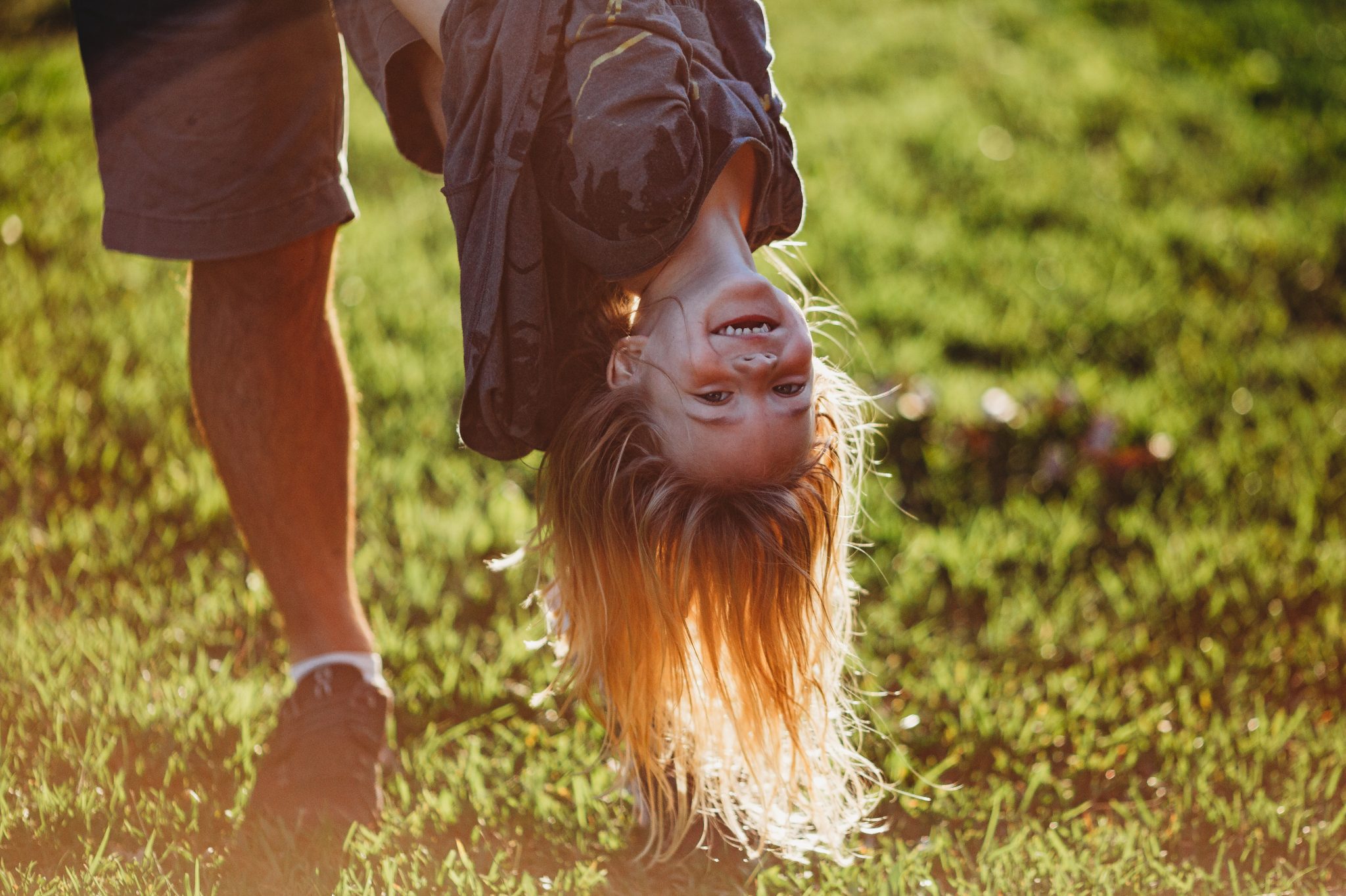Backlit image of young girl hanging upside down, sun lighting up her long hair