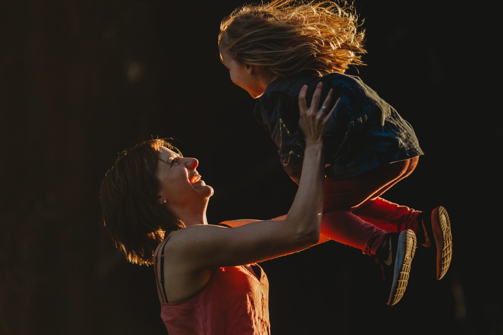 Woman smiling while lifting daughter up into the air