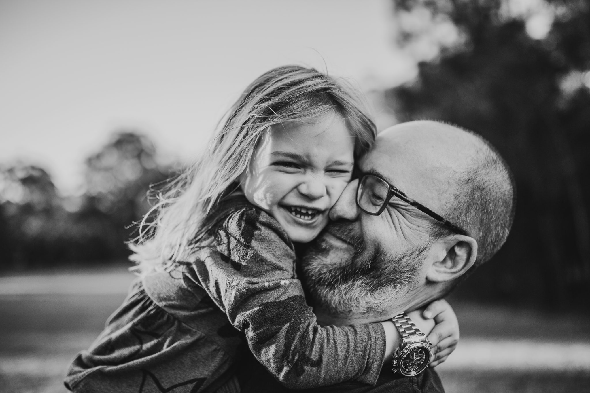 Girl hugging her father's head tightly, slightly squishing his face, both are smiling
