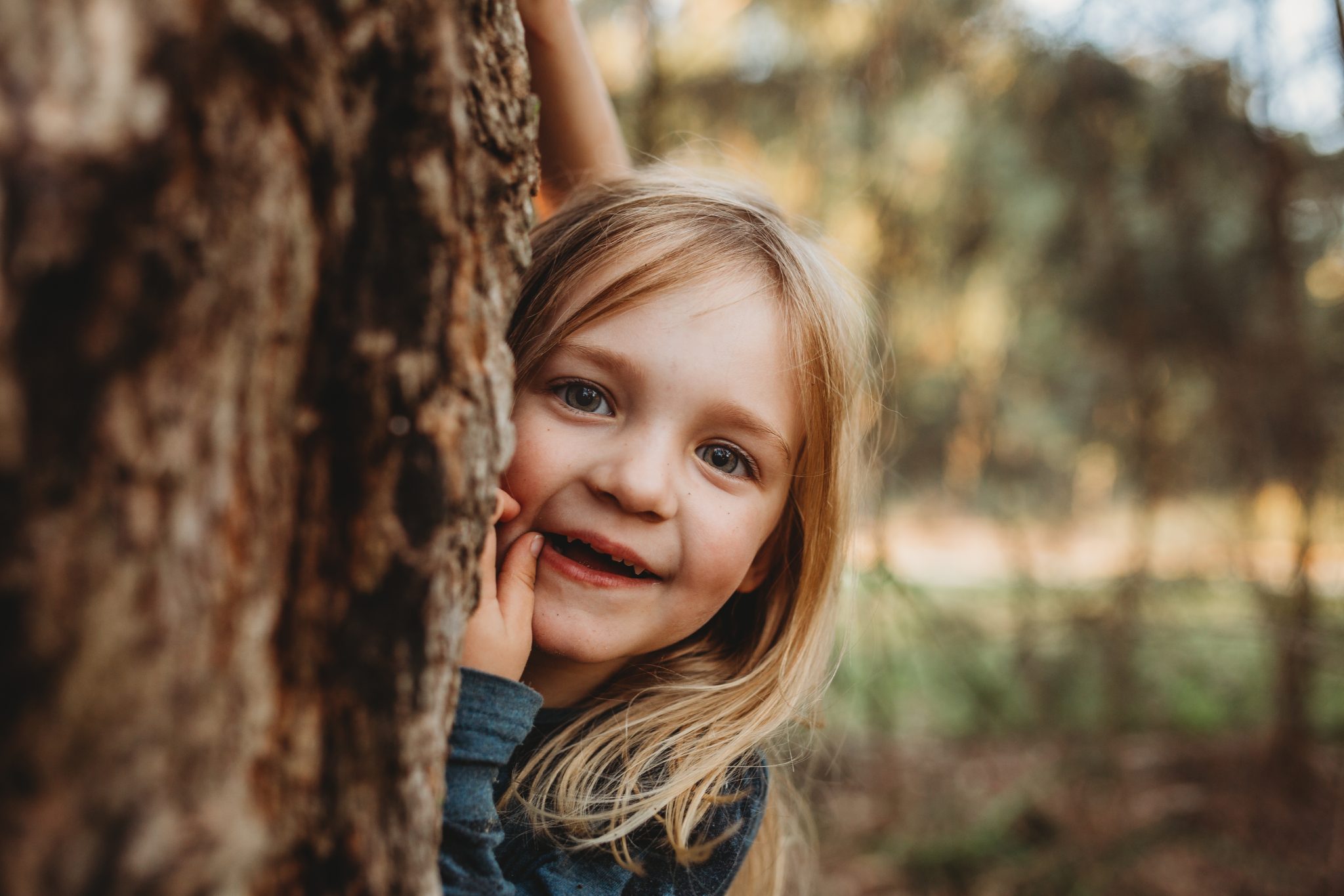 Young girl smiles while peeking out from behind a tree