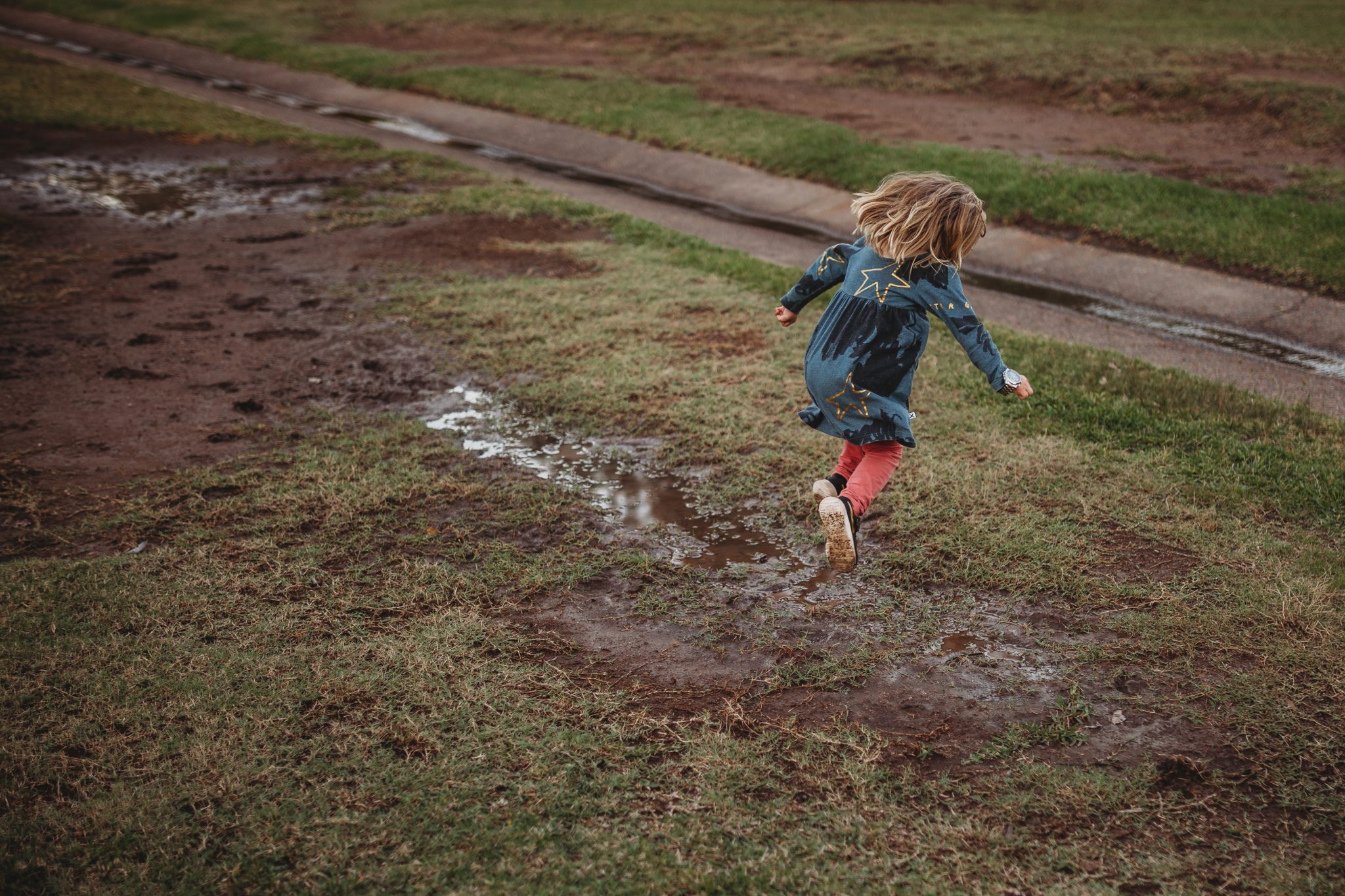 Young girl jumping over muddy puddle