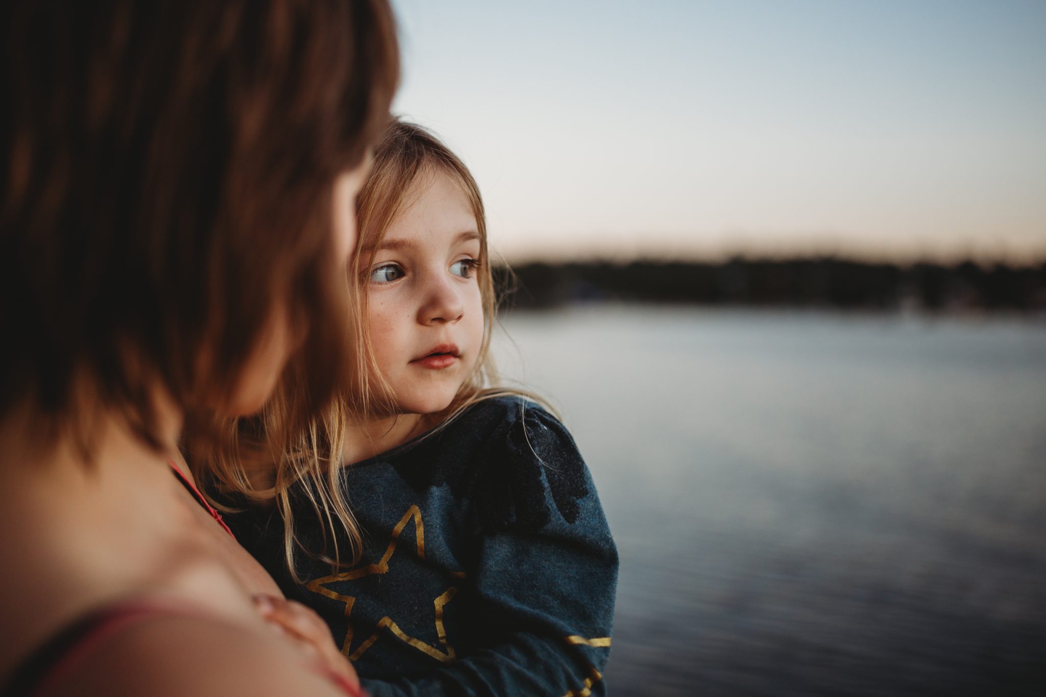 Close up of young girl's face, while in mother's arms at sunset