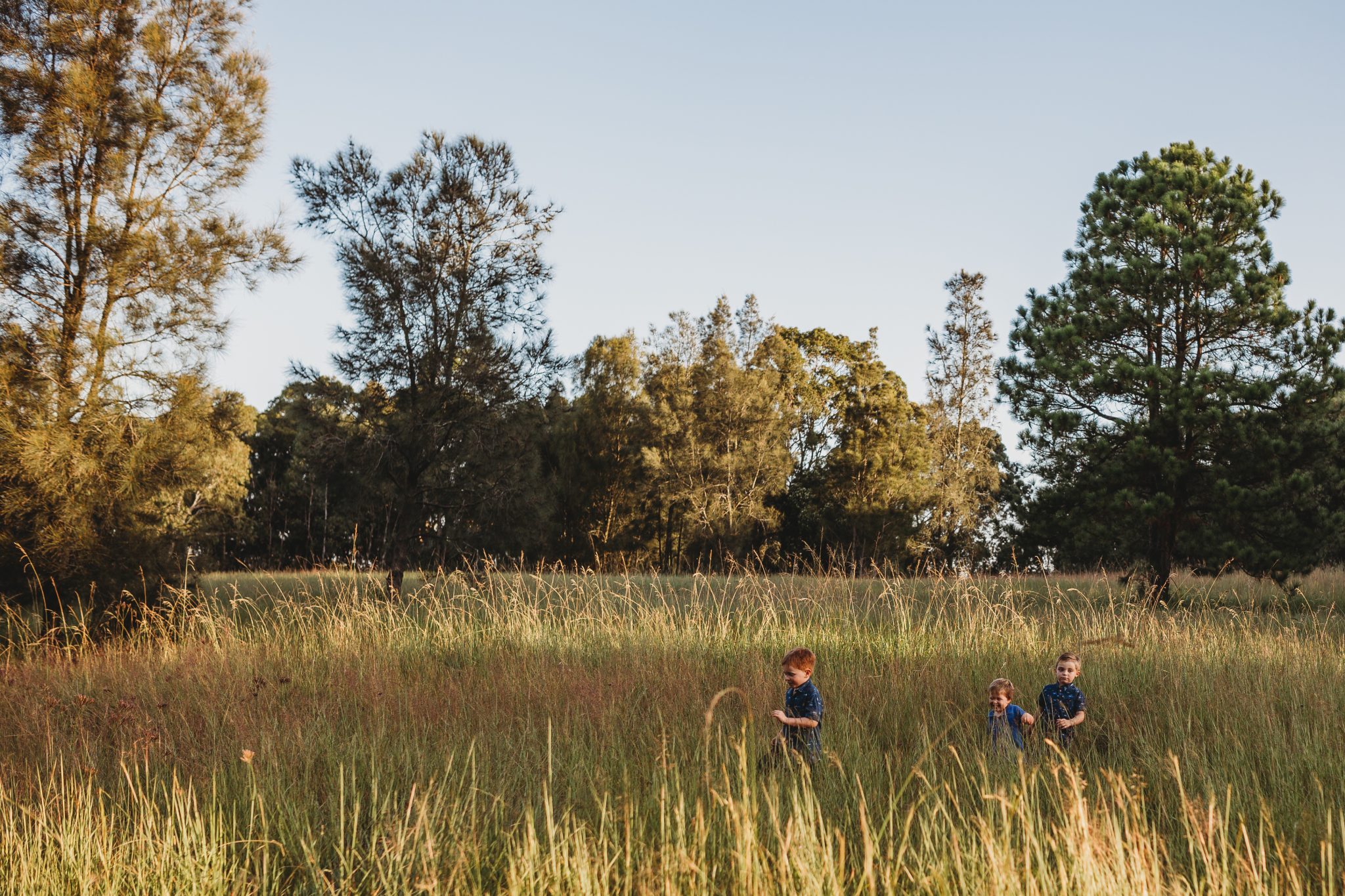 Three young boys running through long grass in Lake Macquarie