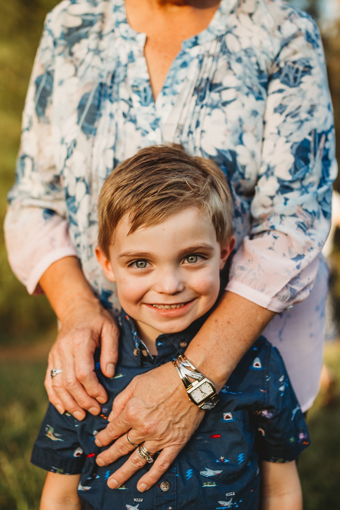 Close up portrait of young boy standing with grandmother's arms around him