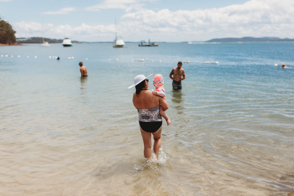Grandmother carrying toddler granddaughter into the water at Shoal Bay beach