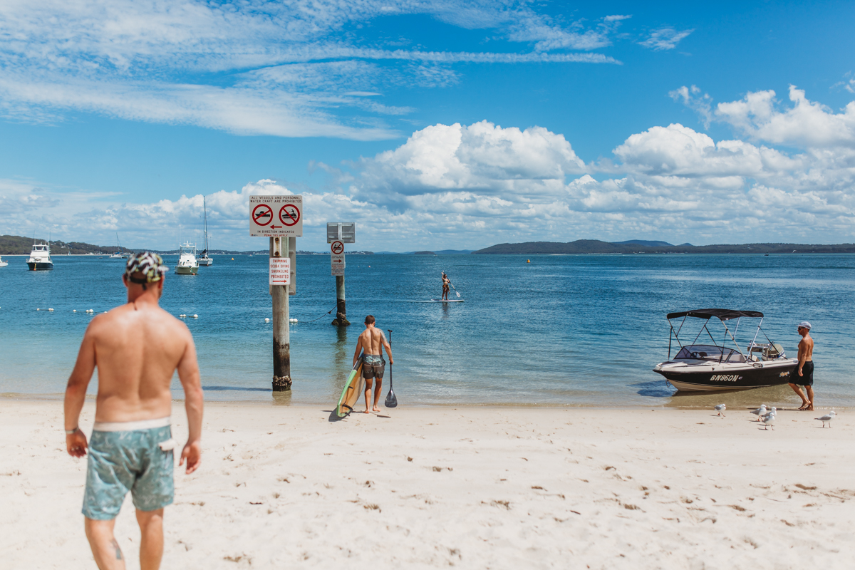 Man at Shoal Bay beach taking stand up paddle board to the water