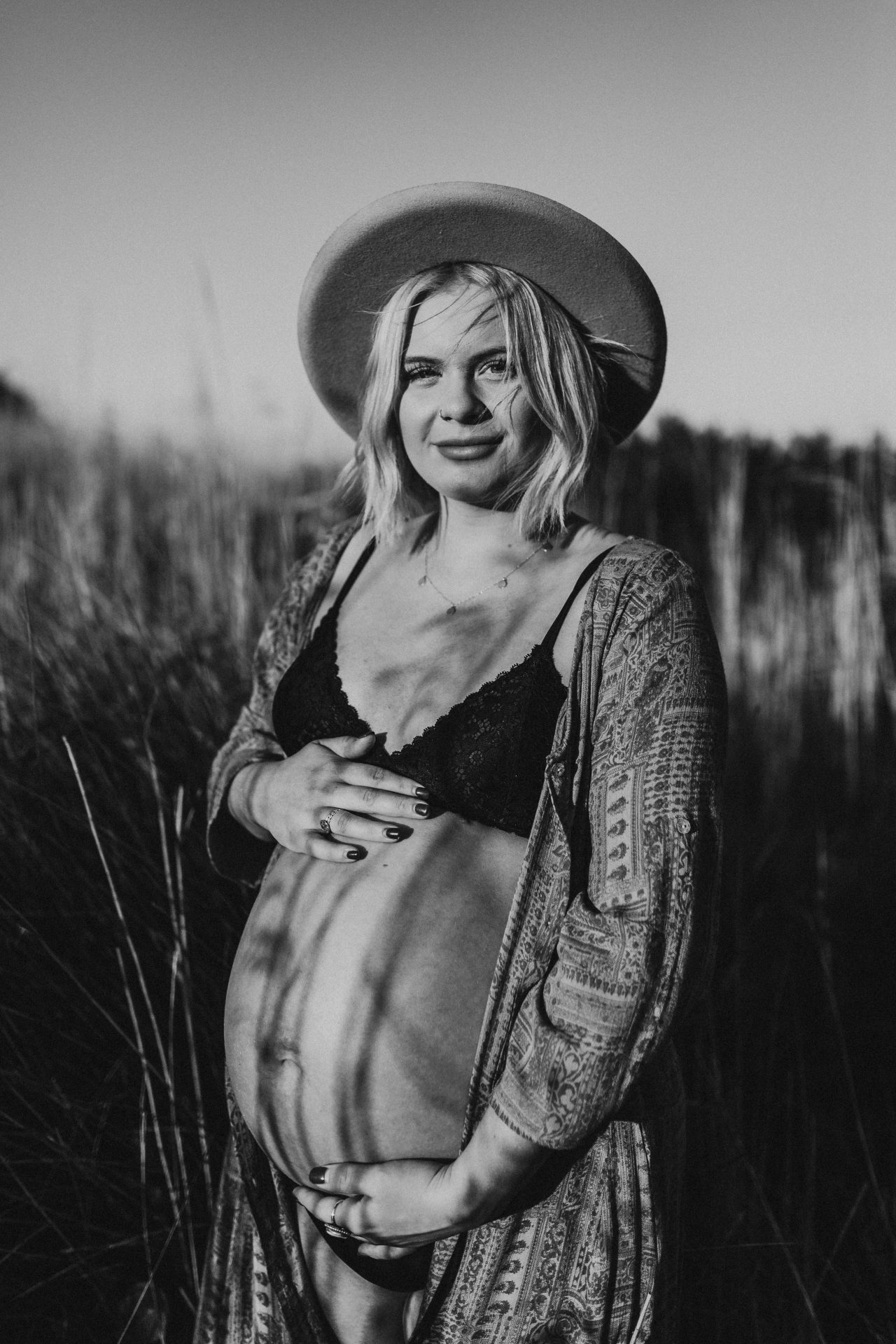 Black and white image of young pregnant woman wearing Lack of Colour hat, looking directly into the camera