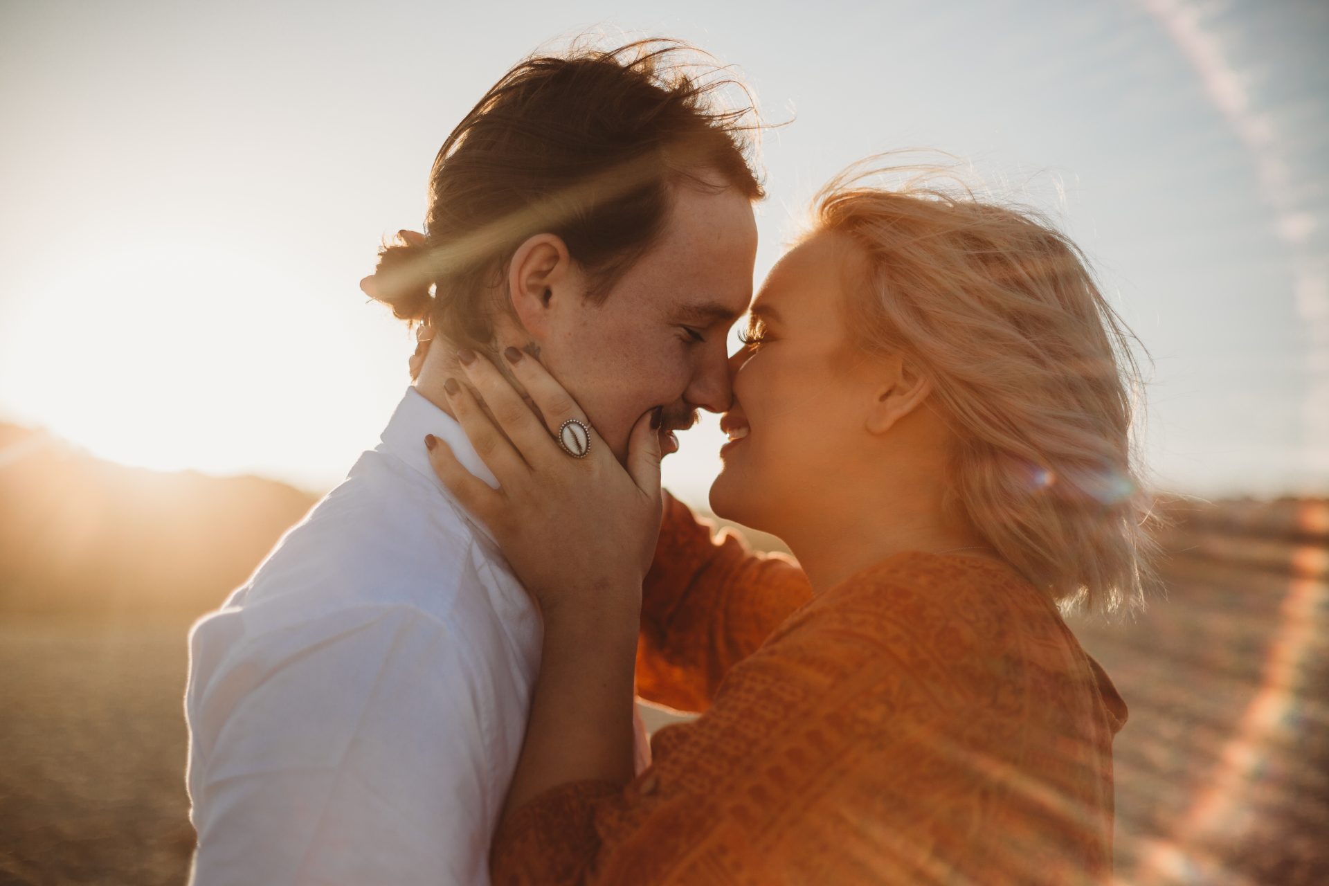 Young couple in an embrace, woman with her hand on her boyfriend's cheek, surrounded by sun flare at sunset