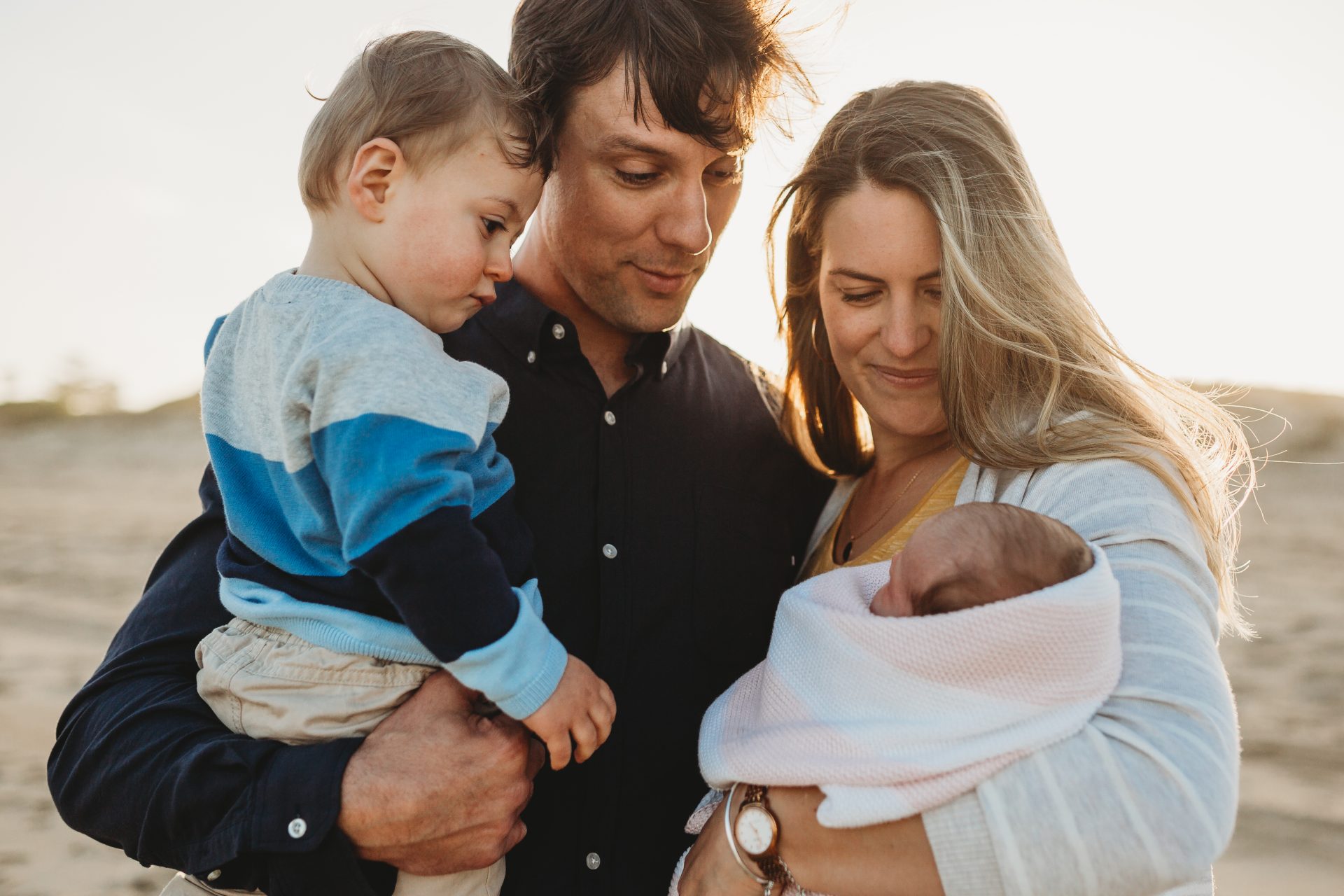 Man, woman and toddler all looking lovingly at newborn baby girl