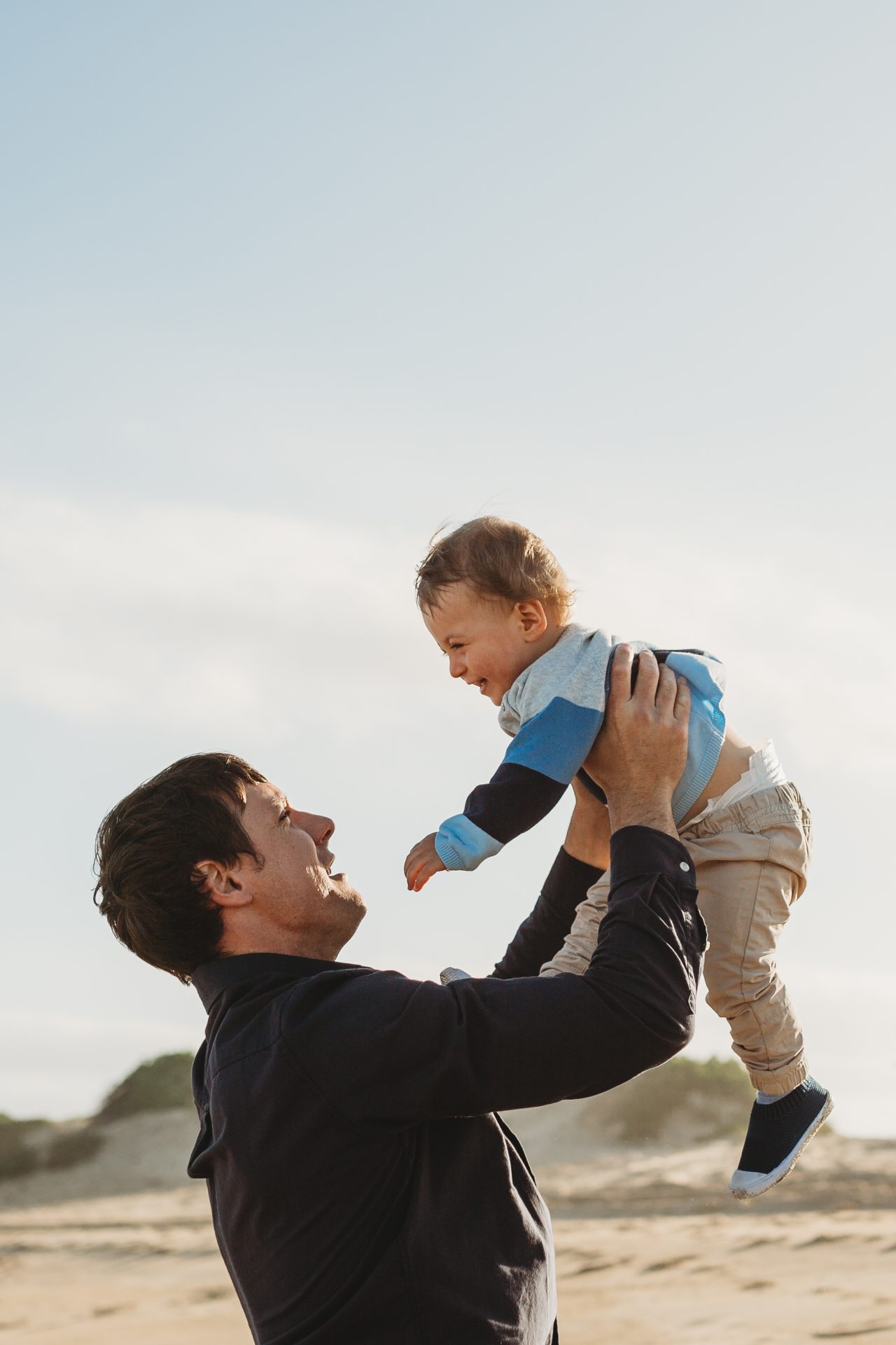 Father holds one year old son up in the air while they're both smiling