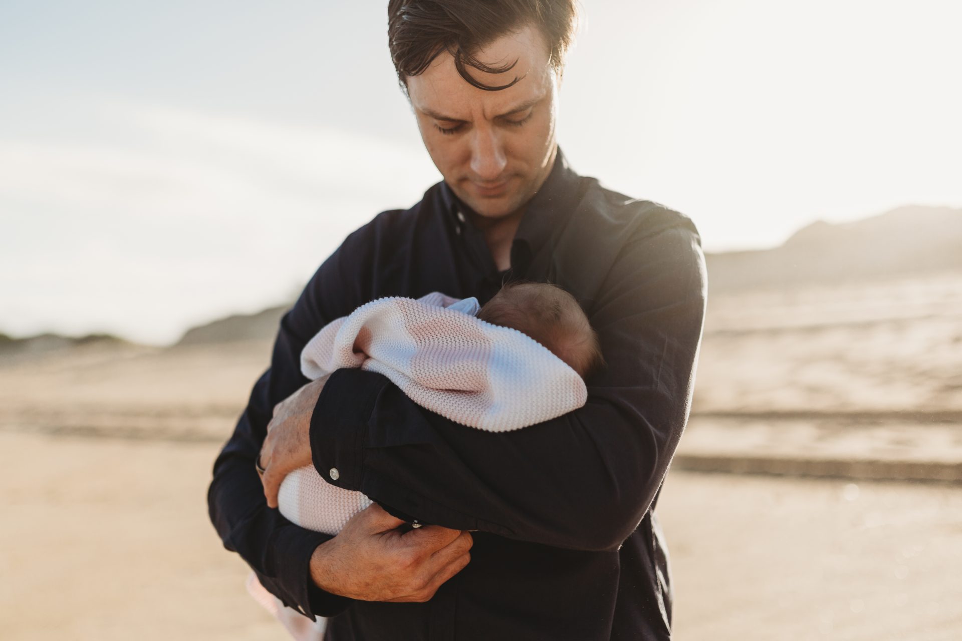 Man on the beach holding his newborn daughter close to his chest