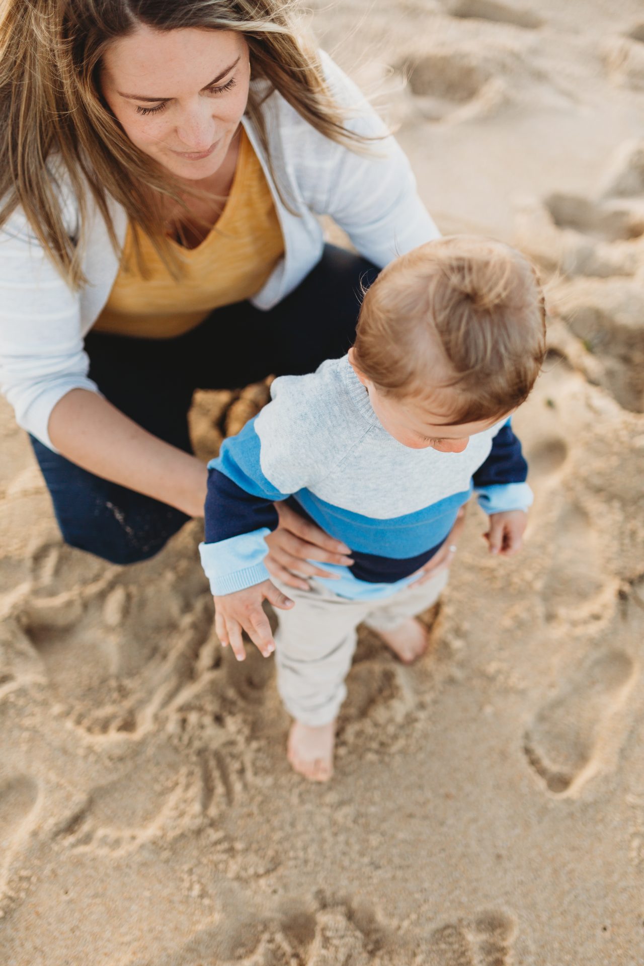 Woman holding toddler as they stand on the sand at the beach