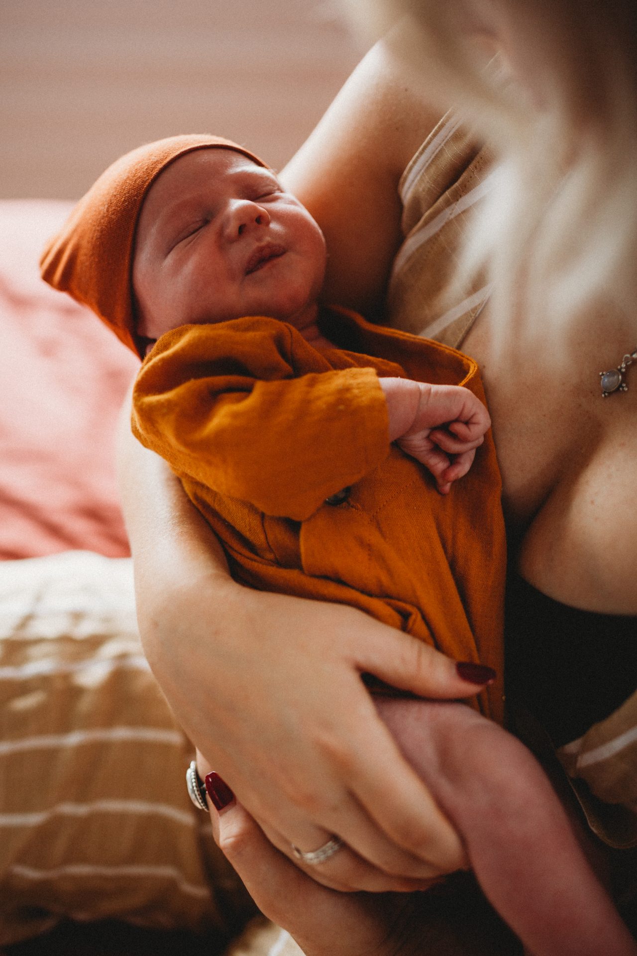 Newborn baby boy, dressed in orange beanie and onesie, cradled in his mother's arms