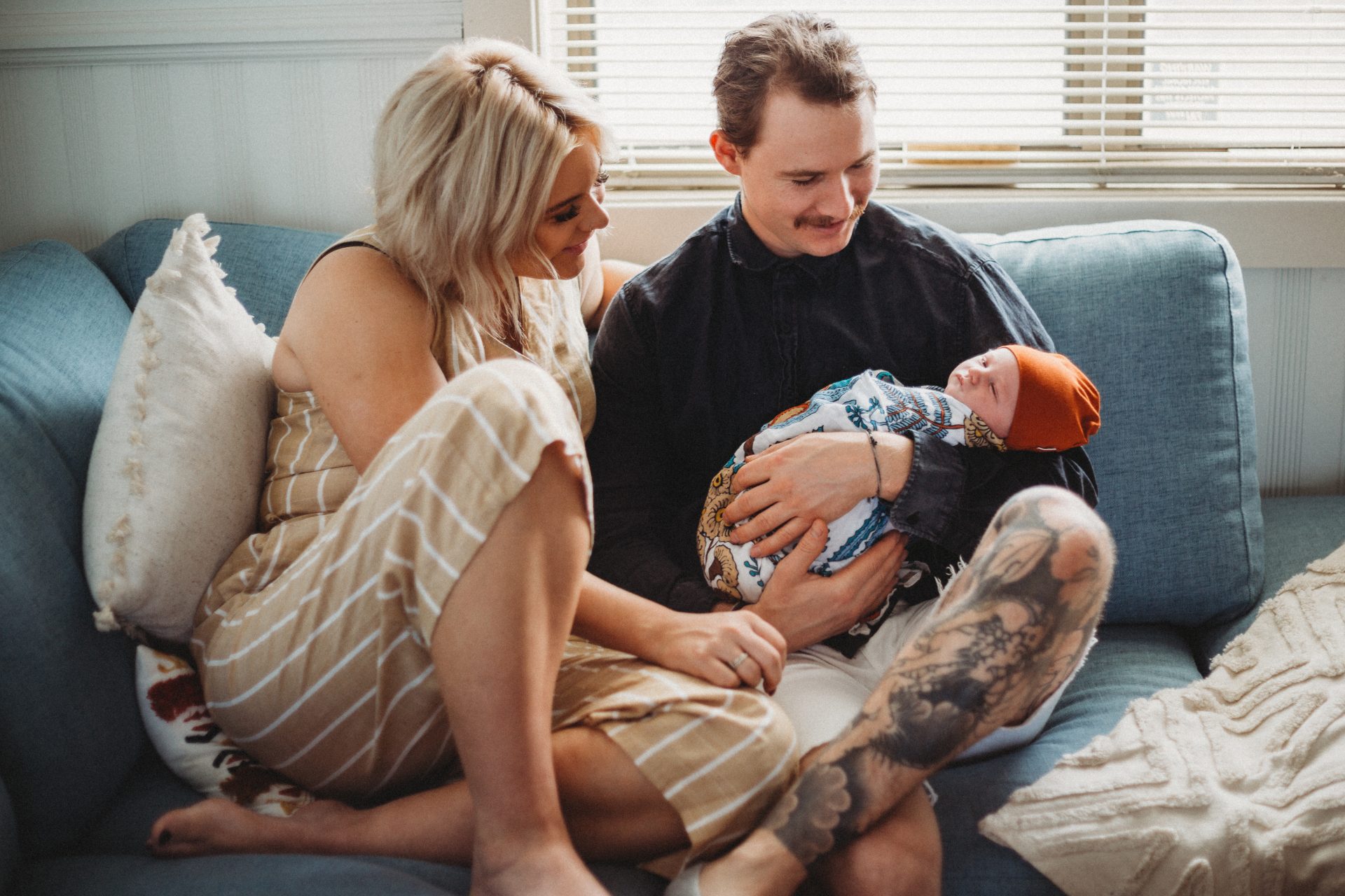 Young couple sitting casually on couch, cuddling newborn baby