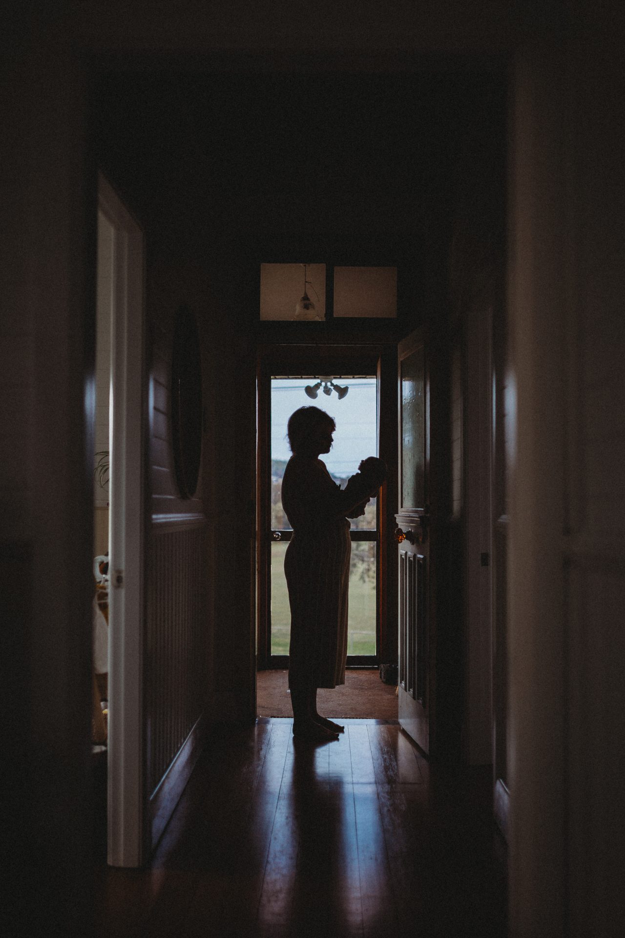 Silhouette of mother and baby in front of a door, down a hallway