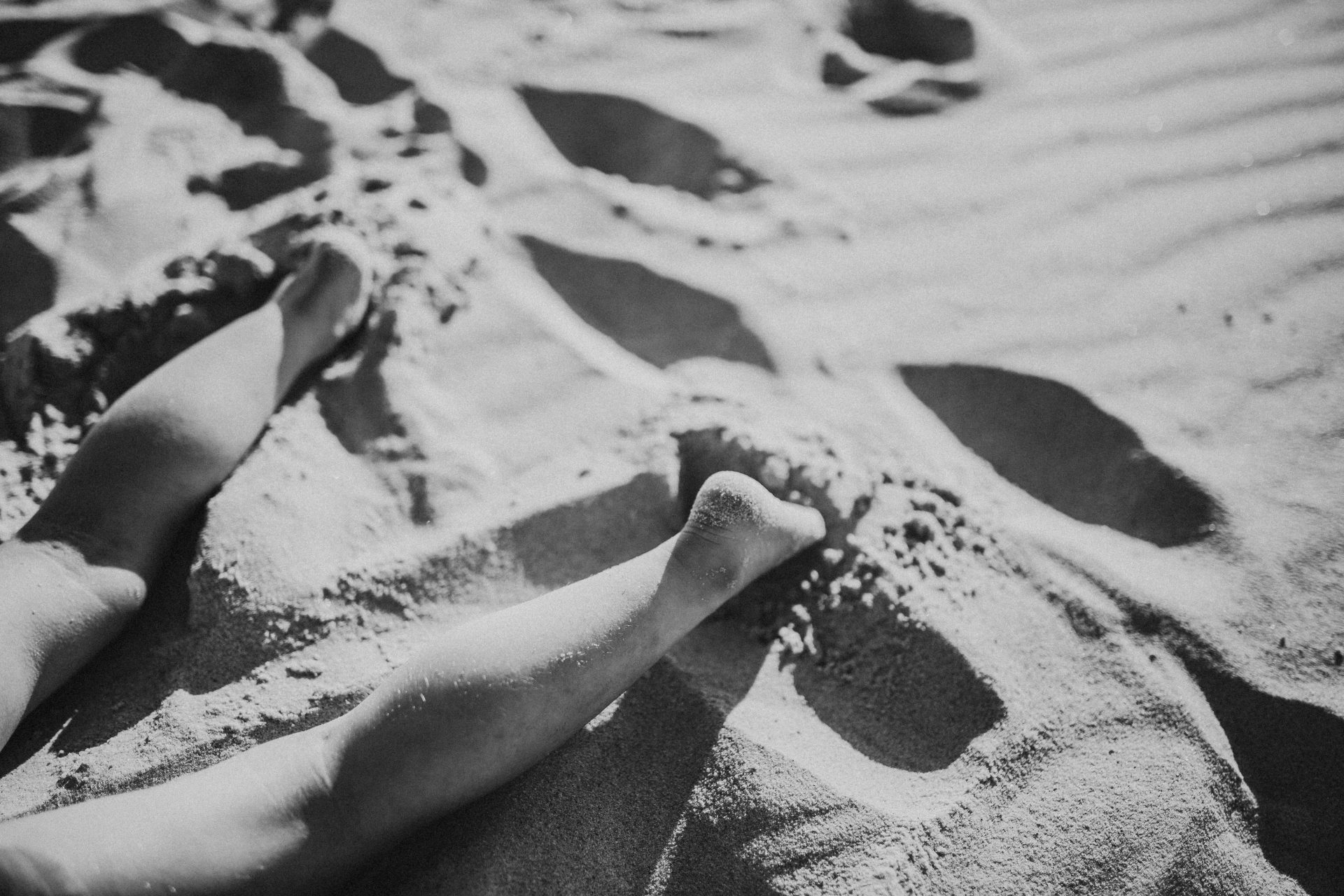 Detail shot of young girl's feet laying in the sand at the beach
