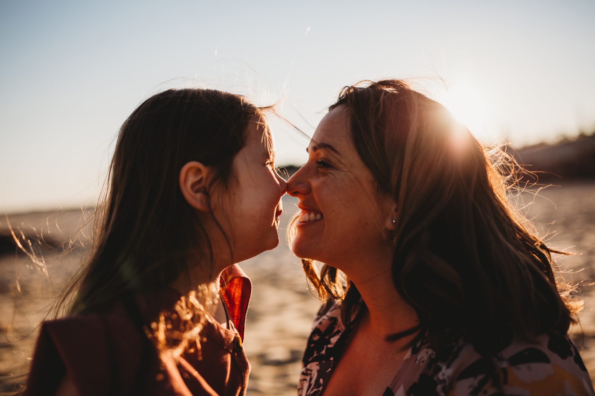 Mother and daughter touching noses as sun sets behind them