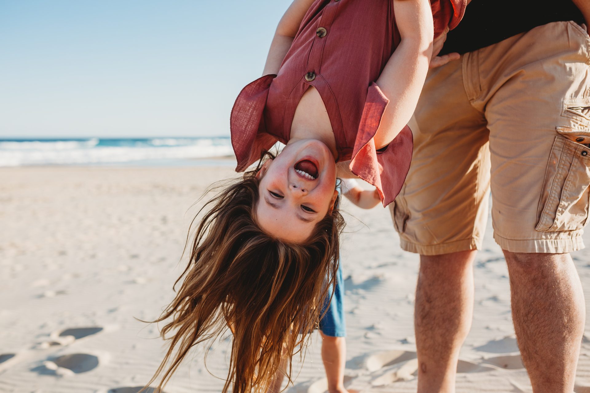 Young girl smiling as she's being swung upside down by her father, her long hair flowing down